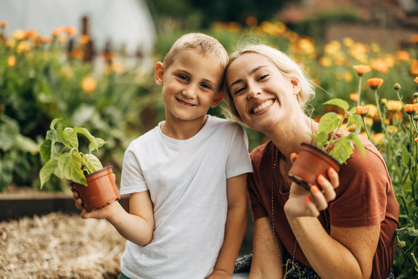Happy mother and son holding potted plants in the garden and smiling to the camera. - Фото, зображення