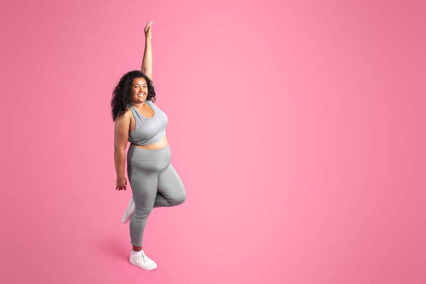 Africaine américaine plus dame taille en vêtements de sport profiter du résultat de l'entraînement, debout isolé sur fond rose, pleine longueur, espace libre. Soins du corps, publicité sportive et offre, fitness, pilates et yoga - Photo, image