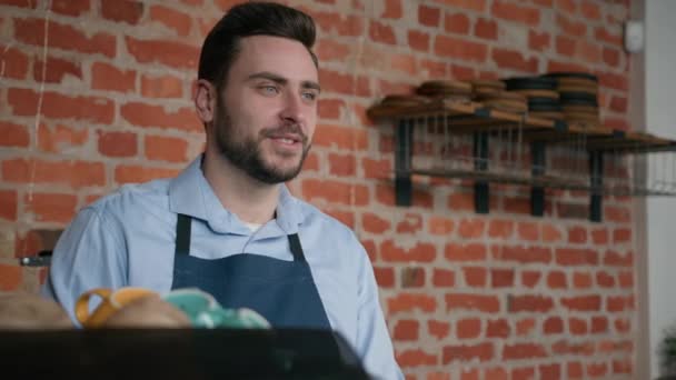 笑顔の優しい白人男性ウェイタープロのバリスタバーテンダーカフェスタッフエプロンで注文を取るカフェテリアカウンターでお客様のコーヒーショップの従業員レストランのクライアントにサービスを提供する従業員 - 映像、動画