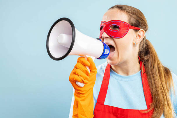 Mulher de limpeza em máscara de herói vermelho, luvas e avental com megafone no fundo azul. Anúncio de informações sobre serviços de limpeza - Foto, Imagem