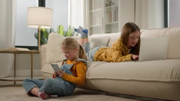 Kinderen en moderne technologie twee gelukkige kinderen meisjes zussen vrienden spelen video online spel samen op laptop telefoon in gezellige woonkamer plezier te spelen met behulp van mobiele en computer applicatie thuis - Video