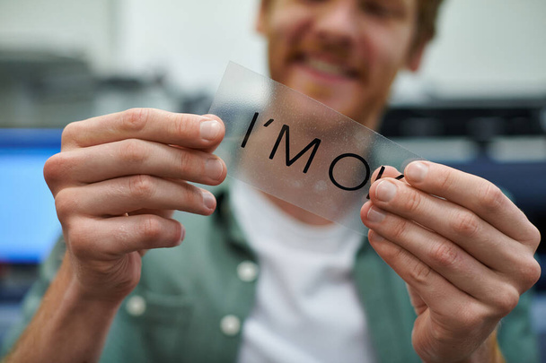 Cropped view of young blurred craftsman holding printing layer with I'm ok lettering in print studio, small business owner working on project, close up, creative process, workflow  - Photo, Image