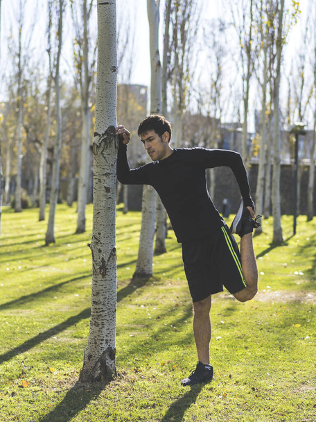 Attraktiver Mann lehnt mit gestrecktem Quadrizeps an einem Baum. - Foto, Bild