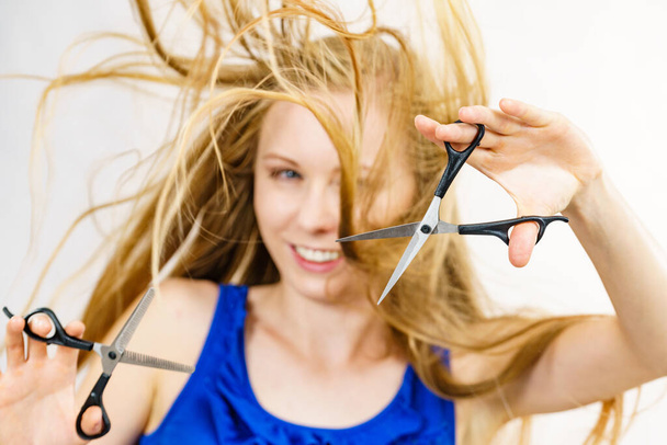 Haircut coiffure haircare concept. Girl with blowing long blond hair holding scissors, showing work tools, normal and thinning shears. - Фото, зображення