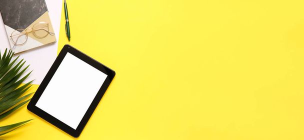 Современный планшетный компьютер, очки и канцелярские принадлежности на желтом фоне с местом для текста - Фото, изображение
