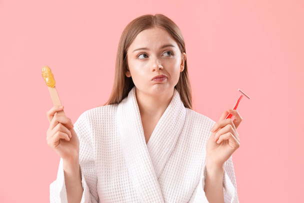 Thoughtful young woman choosing between shaving and sugaring on pink background - Foto, afbeelding