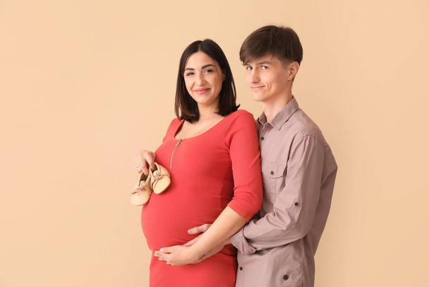 jong zwanger paar met baby laarsjes op beige achtergrond - Foto, afbeelding