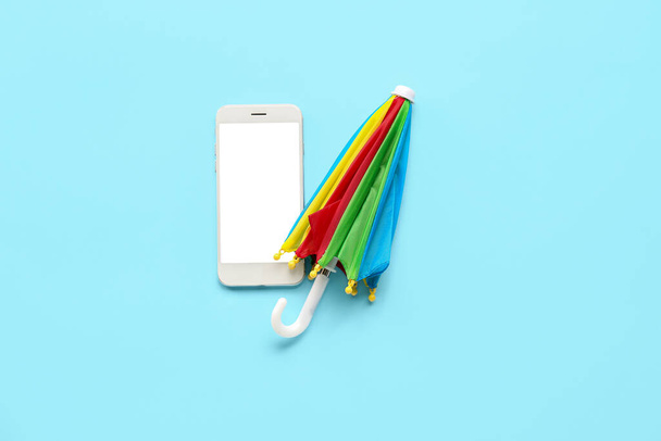 Mobile phone with umbrella on blue background. Weather forecast concept - Zdjęcie, obraz