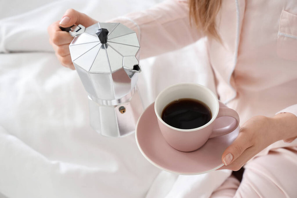 Femme tenant une cafetière geyser et une tasse d'espresso au lit - Photo, image