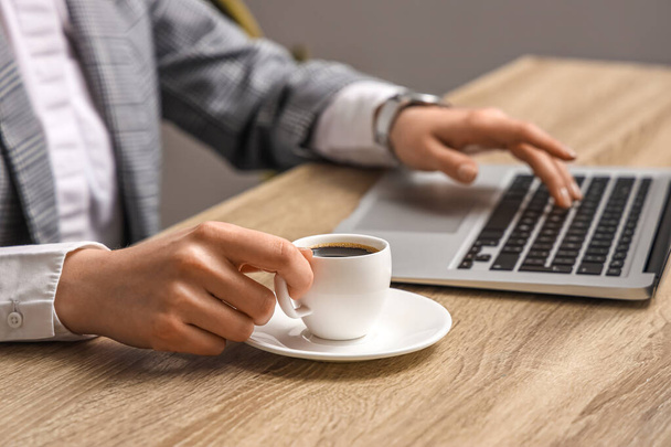 Woman using modern laptop and holding cup of coffee at table - Foto, Imagem