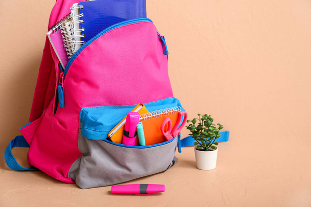 Mochila escolar colorida com cadernos, plantas de sala e marcadores na mesa perto da parede bege - Foto, Imagem