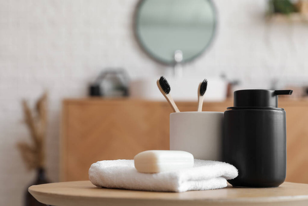 Barra de jabón, dispensador, toalla y taza con cepillos de dientes en la mesa en el baño, primer plano - Foto, imagen