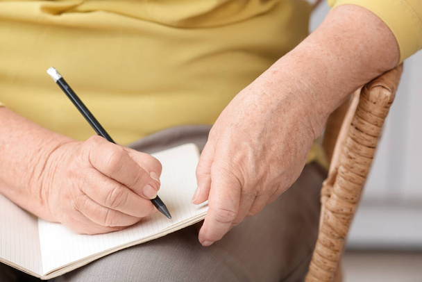 Idősebb nő otthon jegyzetfüzetbe ír, közelkép - Fotó, kép