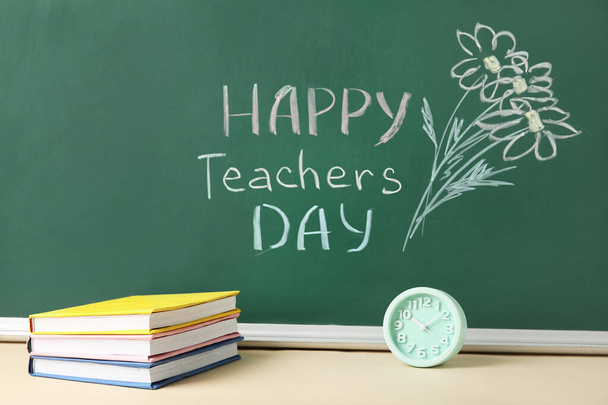 Flores desenhadas e texto HAPPY TEACHERS DIA no quadro verde com livros em sala de aula - Foto, Imagem
