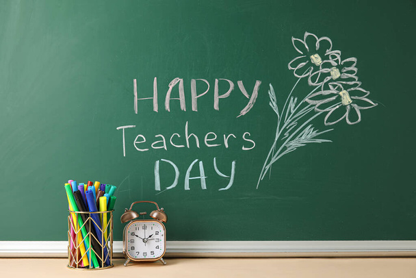 Drawn flowers and text HAPPY TEACHERS DAY on green chalkboard with markers holder in classroom - Foto, afbeelding
