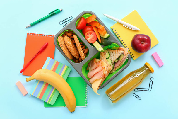 Канцелярские принадлежности, напитки и обеденная коробка с вкусной едой на синем фоне - Фото, изображение