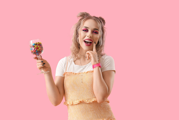 Mujer joven con vaso de caramelos sobre fondo rosa - Foto, Imagen