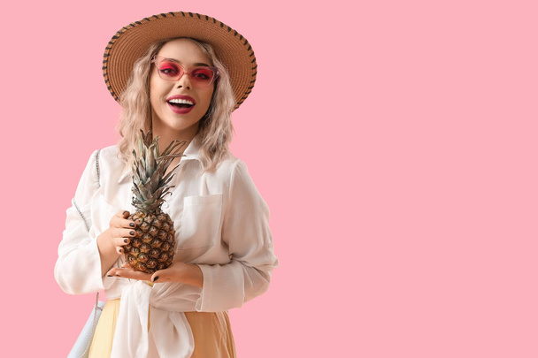 Молода жінка в сонцезахисних окулярах з ананасом на рожевому фоні - Фото, зображення
