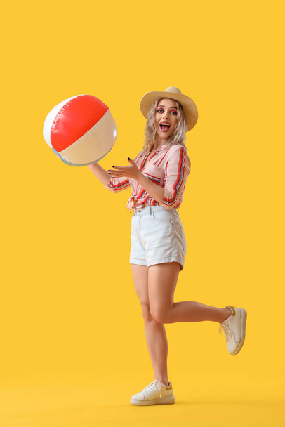 Young woman with beach ball on yellow background - Fotoğraf, Görsel