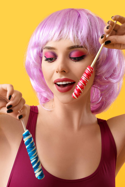Young woman in wig with lollipops on yellow background, closeup - Foto, immagini