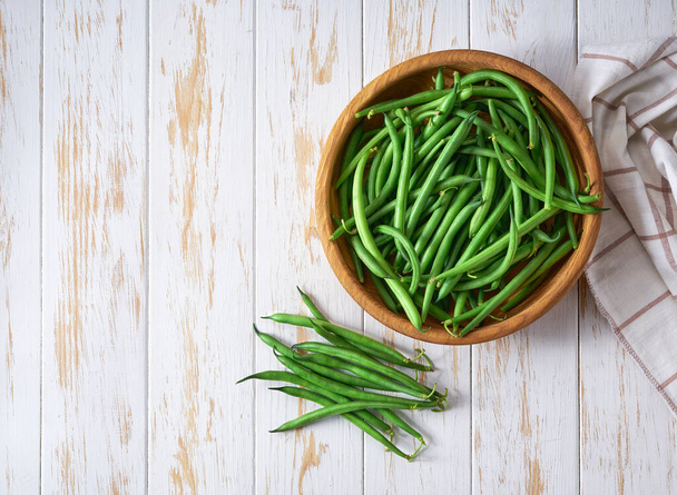 fresh green beans in a bowl on a white wooden table, top view. - Fotó, kép