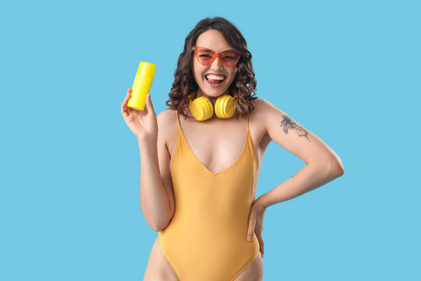 Mujer joven en traje de baño con crema protector solar sobre fondo azul - Foto, imagen