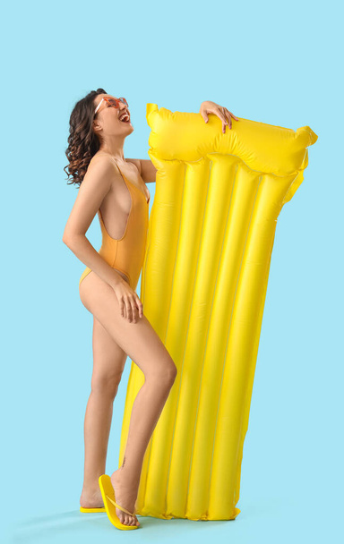 Young woman in swimsuit with inflatable mattress on blue background - Photo, Image