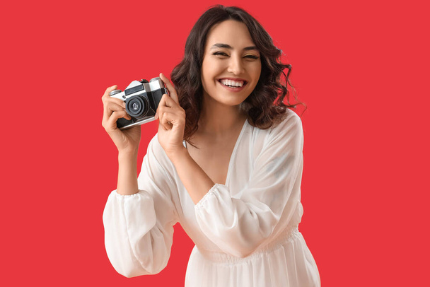 Young woman with photo camera on red background - Photo, Image