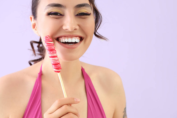Young woman in swimsuit with lollipop on lilac background, closeup - Foto, imagen