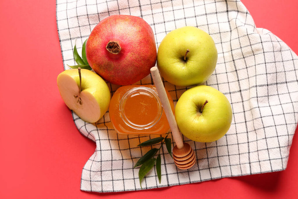 Jar of honey, pomegranate and apples for Rosh Hashanah celebration (Jewish New Year) on red background - Photo, image