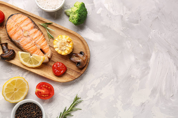 Wooden board with tasty grilled salmon steak and vegetables on grunge background - Фото, зображення