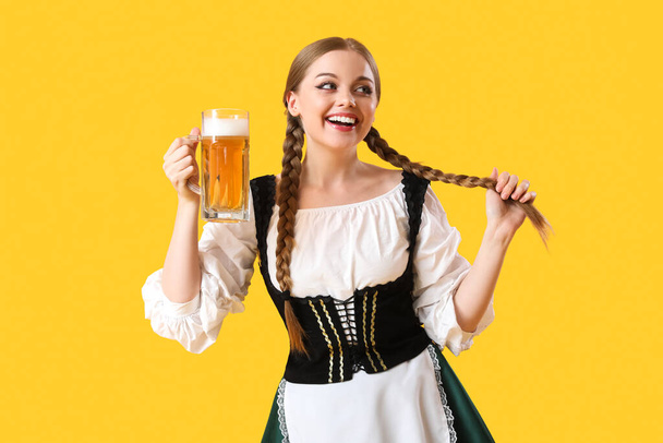 Beautiful Octoberfest waitress with beer on yellow background - Photo, Image