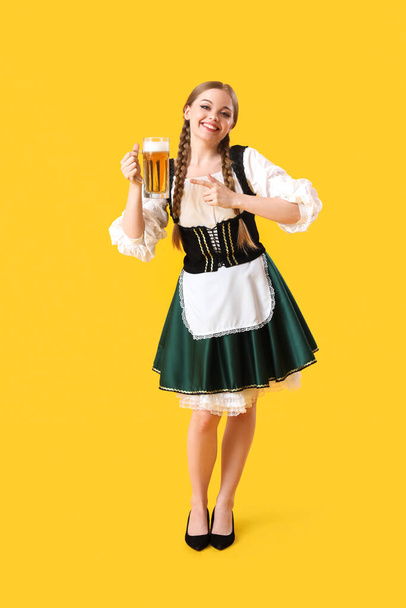 Krásná Oktoberfest servírka ukazuje na pivo na žlutém pozadí - Fotografie, Obrázek