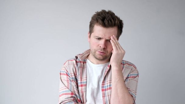 Eurooppalainen nuori mies kärsii päänsärystä ja hieroo ohimojaan. Studiokuva - Valokuva, kuva