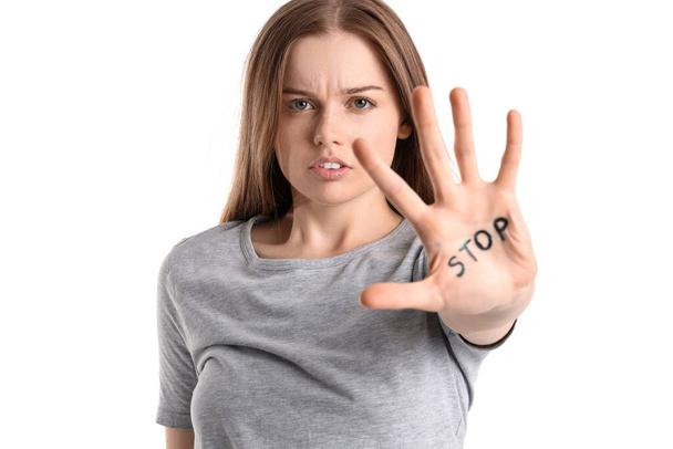 Νεαρή γυναίκα με λέξη STOP γραμμένο στην παλάμη της σε λευκό φόντο - Φωτογραφία, εικόνα