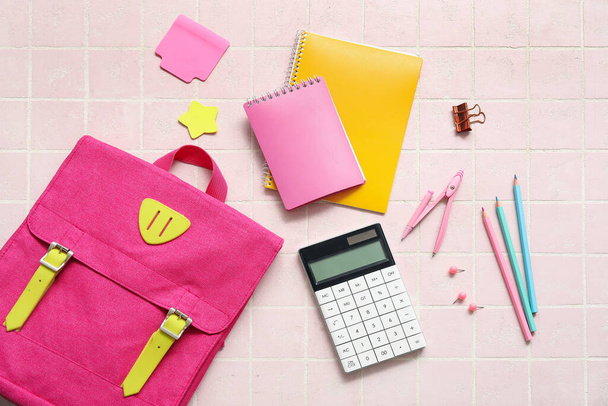 Mochila escolar rosa con calculadora, cuadernos y lápices sobre fondo de baldosa clara - Foto, Imagen