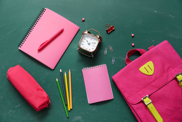 Růžový školní batoh s poznámkovými bloky, pouzdrem na tužky a budíkem na zeleném pozadí - Fotografie, Obrázek