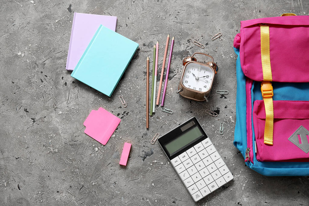 Kleurrijke schoolrugzak met notitieboekjes, wekker en rekenmachine op grijze grunge achtergrond - Foto, afbeelding