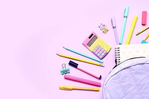 Mochila con calculadoras y diferentes artículos de papelería sobre fondo lila - Foto, imagen