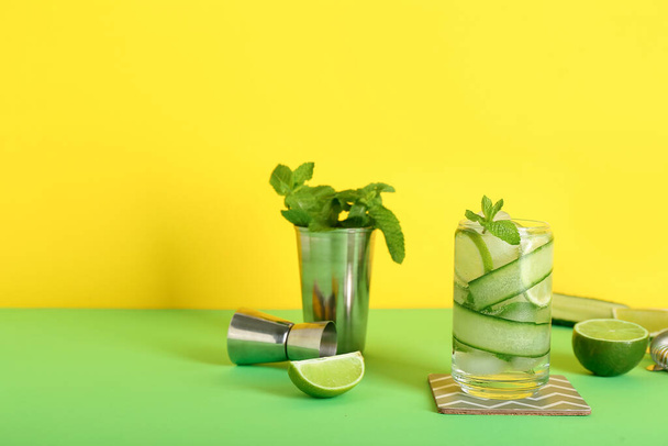 Glass of cucumber mojito with bartender tools on color background - Foto, imagen