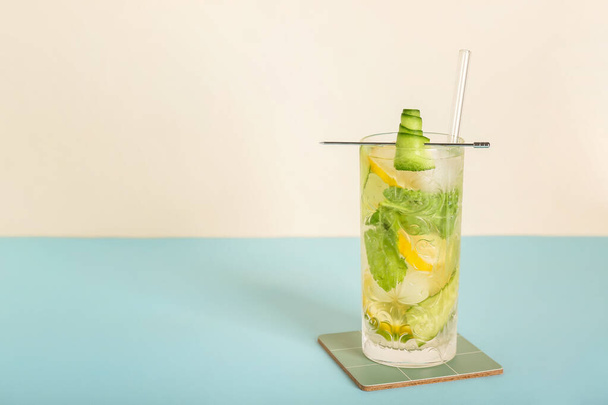 Glass of mojito with lemon, cucumber and ice cubes on blue table near white wall - Photo, image