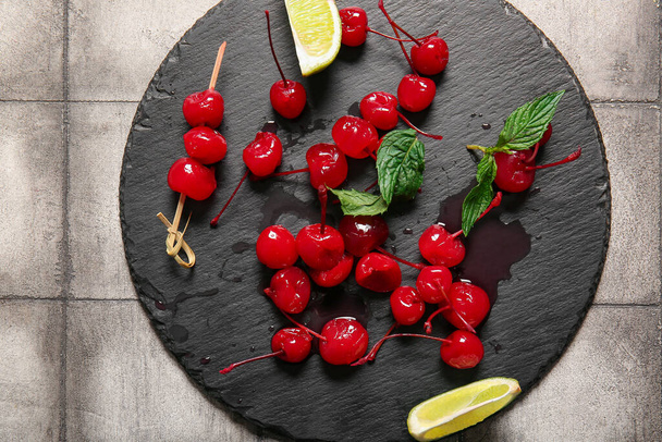 Slate board with tasty maraschino cherries on grey tile background - Foto, immagini