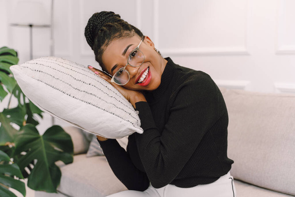 Portrait of attractive black woman smiling and happy on white background, African American woman wearing black top playing with pillow - Foto, Imagem