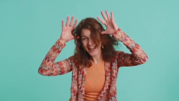 Funny comical playful young woman making silly facial expressions and grimacing, fooling around, showing tongue, idiotic expression. Girl isolated alone on blue studio background. People lifestyles - Footage, Video