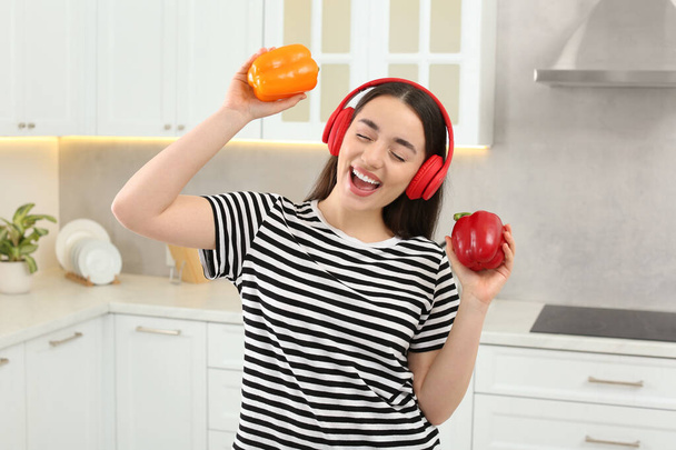 Happy woman in headphones listening music and dancing with bell peppers in kitchen - Photo, Image