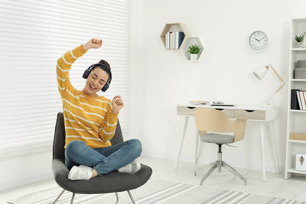 Happy woman in headphones enjoying music and dancing on cosy armchair at home - Foto, immagini