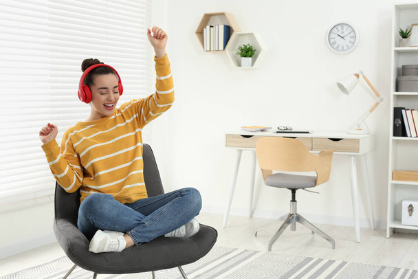 Szczęśliwa kobieta w słuchawkach korzystających z muzyki i tańca na przytulnym fotelu w domu - Zdjęcie, obraz