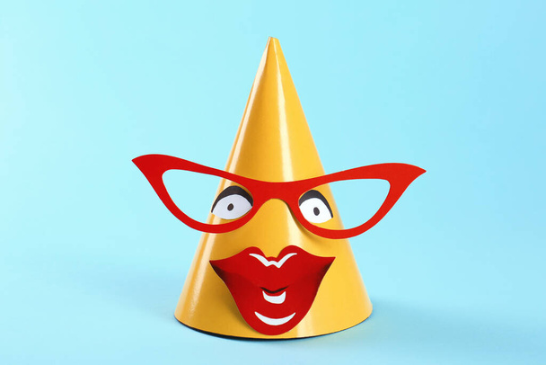 Handmade party hat with funny face on light blue background - Фото, зображення