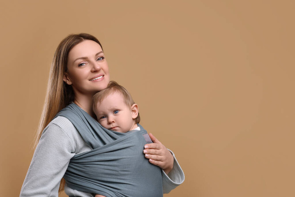 Mother holding her child in baby wrap on light brown background. Space for text - Photo, image