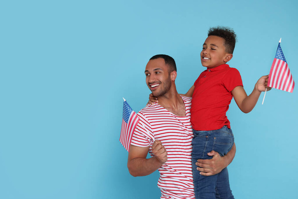 4th of July - Independence Day of USA. Happy man and his son with American flags on light blue background, space for text - Фото, изображение